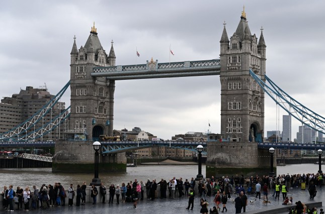 TOPSHOT - Members of the public stand in the queue on the South Bank of the River Thames, alongside Tower Bridge, as they wait in line to pay their respects to the late Queen Elizabeth II, in London on September 15, 2022. - Queen Elizabeth II will lie in state until 0530 GMT on September 19, a few hours before her funeral, with huge queues expected to file past her coffin to pay their respects. (Photo by CARL DE SOUZA / AFP) (Photo by CARL DE SOUZA/AFP via Getty Images)