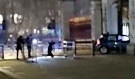 Video grab from the aftermath of the dramatic moment a car crashed into Buckingham Palace has been captured on camera. Footage of the incident shows the car, with its hazard lights on, rammed into the main entrance gates of the royal residence in Westminster, central London. Photo released March 10 2024. See SWNS story SWTPpalace.A man is on the ground on his knees behind the car, and an armed police officer can be heard yelling: ?Keep your hands on top of your head!? The Met Police said a man had been arrested on suspicion of criminal damage.