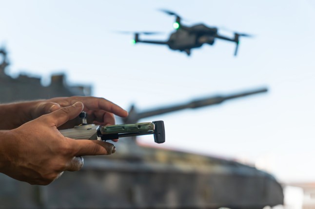 a man with a UAV control panel in his hands, a drone flying above the tank in the background in nature. help of reconnaissance drones in modern warfare.